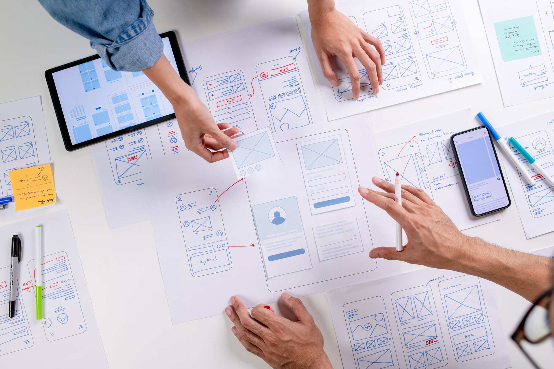 UX/UI designers discussing and brainstorming on wireframes for a website and mobile app prototype, surrounded by sketches of user flow and design tools, in the concept of website and mobile application design concept.